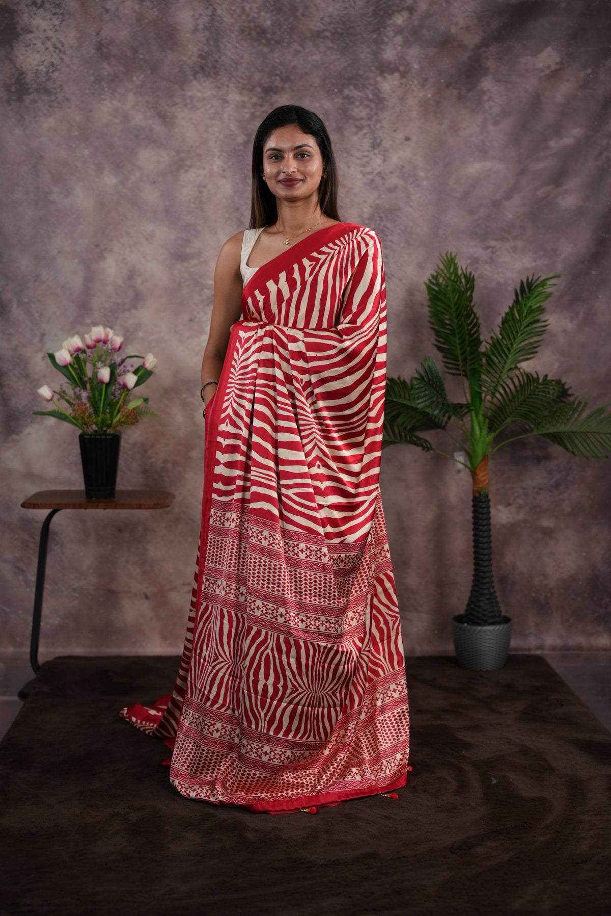 Red Colour satin model saree featuring Zibra print on body. Ajrak & zibra print on pallu with jhumka tassels, comes with contrast plain blouse piece.