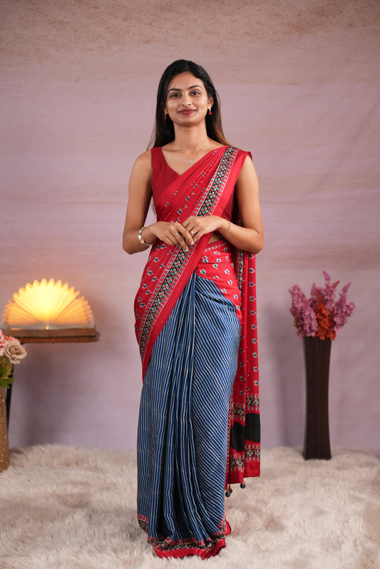 Red and blue colour satin modal saree featuring stripes on the body, Ajrakh prints on the border & polka dots with jhumka tassels on the pallu, paired with a matching Ajrakh printed blouse piece.