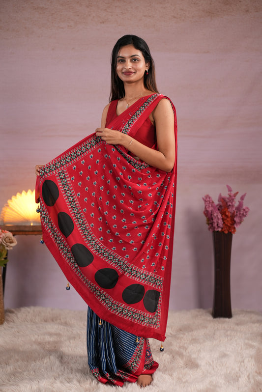 Red and blue colour satin modal saree featuring stripes on the body, Ajrakh prints on the border & polka dots with jhumka tassels on the pallu, paired with a matching Ajrakh printed blouse piece.