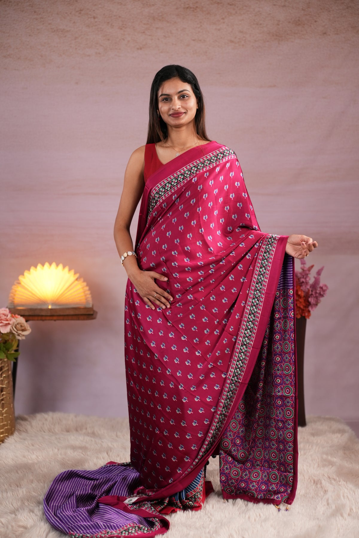 Plum and Purple colour satin modal saree featuring stripes on the body, Ajrakh prints on the border & polka dots with jhumka tassels on the pallu, paired with a matching Ajrakh printed blouse piece.