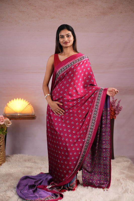 Plum and Purple colour satin modal saree featuring stripes on the body, Ajrakh prints on the border & polka dots with jhumka tassels on the pallu, paired with a matching Ajrakh printed blouse piece.