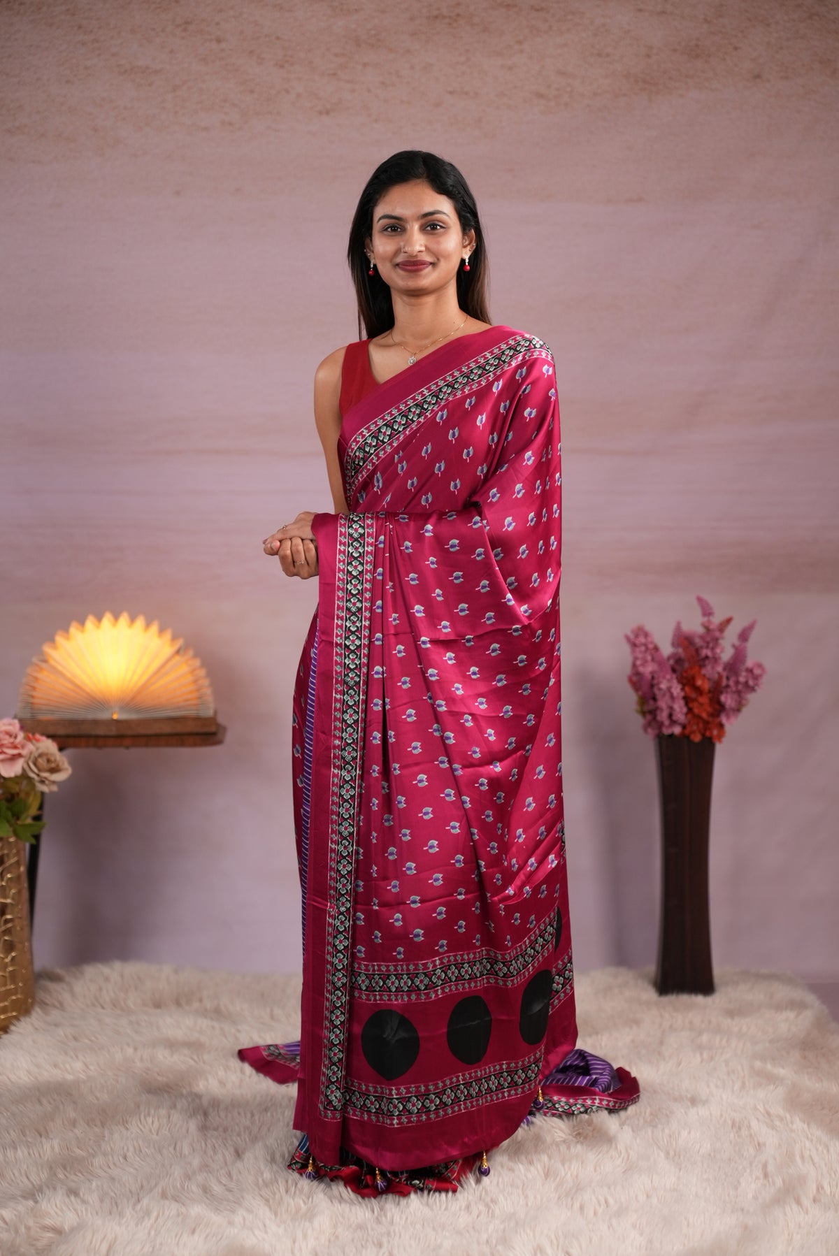 Plum and Purple colour satin modal saree featuring stripes on the body, Ajrakh prints on the border & polka dots with jhumka tassels on the pallu, paired with a matching Ajrakh printed blouse piece.