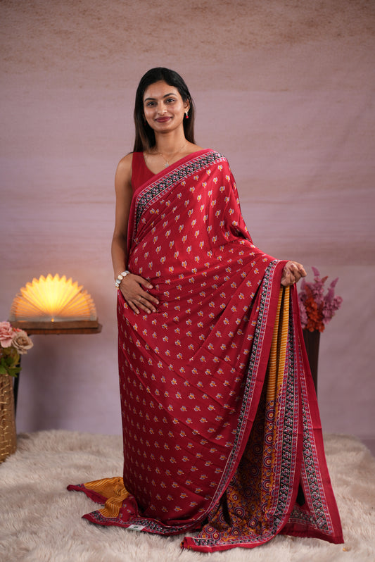 Reddish Maroon and Mustard Yellow colour satin modal saree featuring stripes on the body, Ajrakh prints on the border & polka dots with jhumka tassels on the pallu, paired with a matching Ajrakh printed blouse piece.