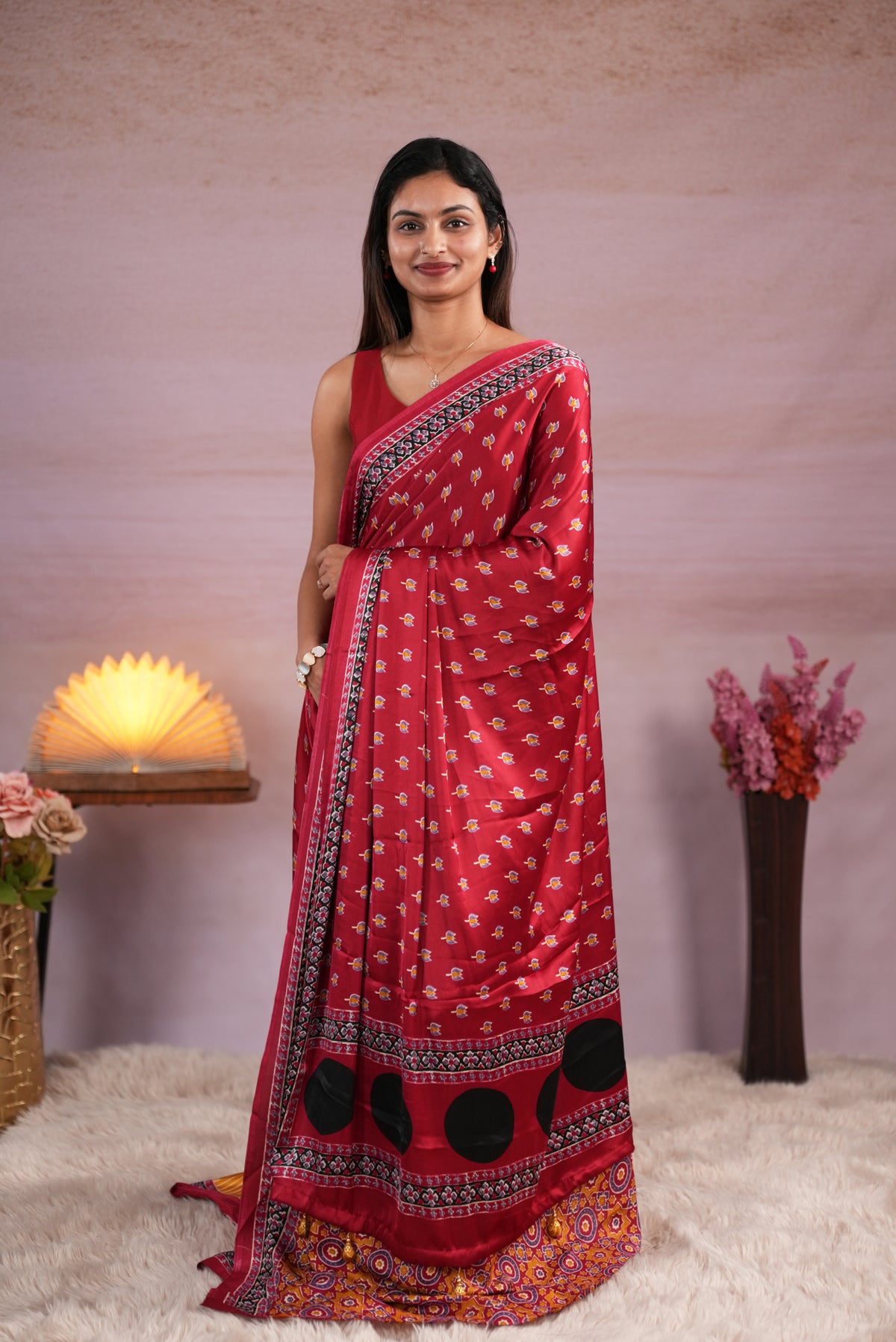 Reddish Maroon and Mustard Yellow colour satin modal saree featuring stripes on the body, Ajrakh prints on the border & polka dots with jhumka tassels on the pallu, paired with a matching Ajrakh printed blouse piece.