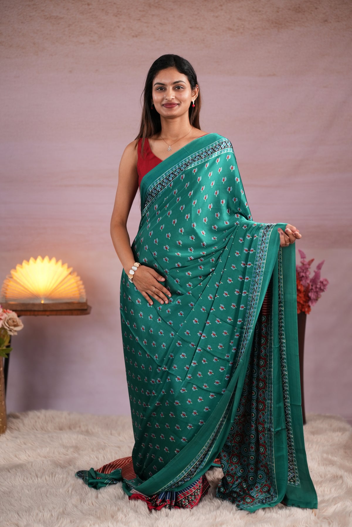 Peacock Green and Rust Orange colour satin modal saree featuring stripes on the body, Ajrakh prints on the border & polka dots with jhumka tassels on the pallu, paired with a matching Ajrakh printed blouse piece.