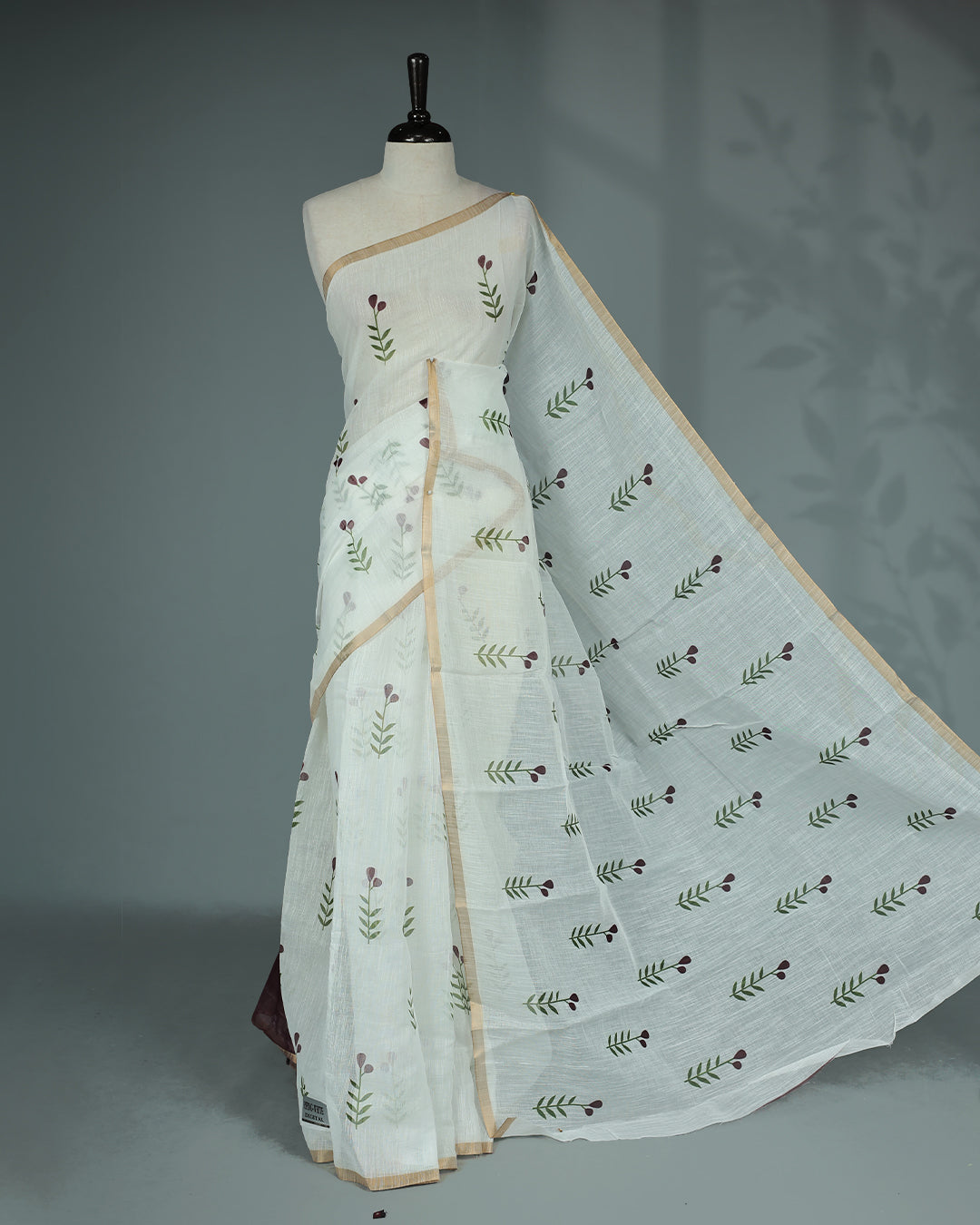 Off-white linen saree featuring beautiful Brown floral and leafy prints on the body, complemented by a tissue piping border and a contrasting pallu. Paired with a matching blouse piece.