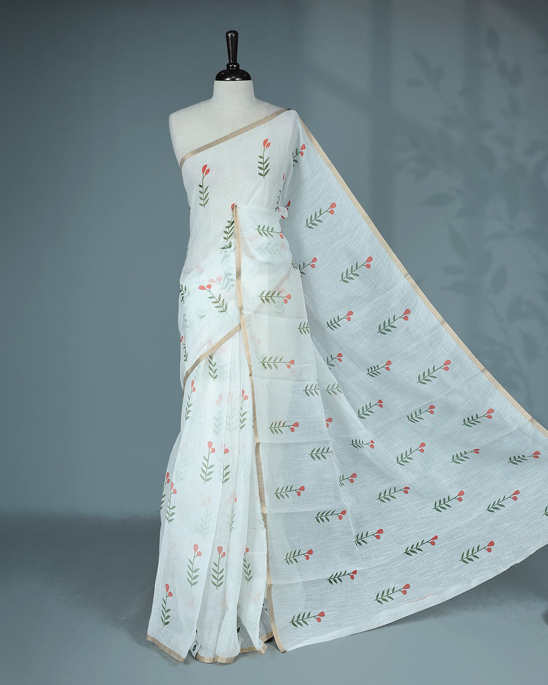 Off-white linen saree featuring beautiful orange floral and leafy prints on the body, complemented by a tissue piping border and a contrasting pallu. Paired with a matching blouse piece.