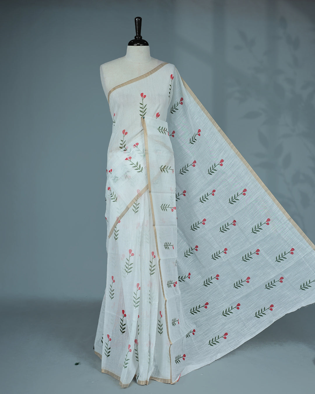 Off-white linen saree featuring beautiful Red floral and leafy prints on the body, complemented by a tissue piping border and a contrasting pallu. Paired with a matching blouse piece.