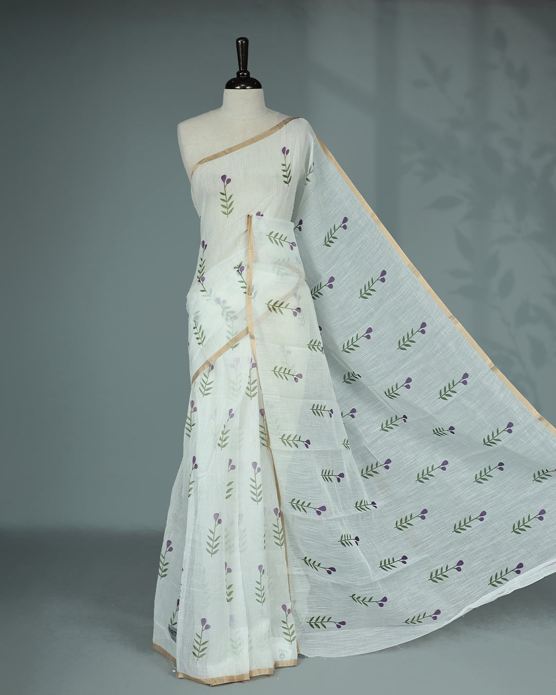 Off-white linen saree featuring beautiful Purple floral and leafy prints on the body, complemented by a tissue piping border and a contrasting pallu. Paired with a matching blouse piece.