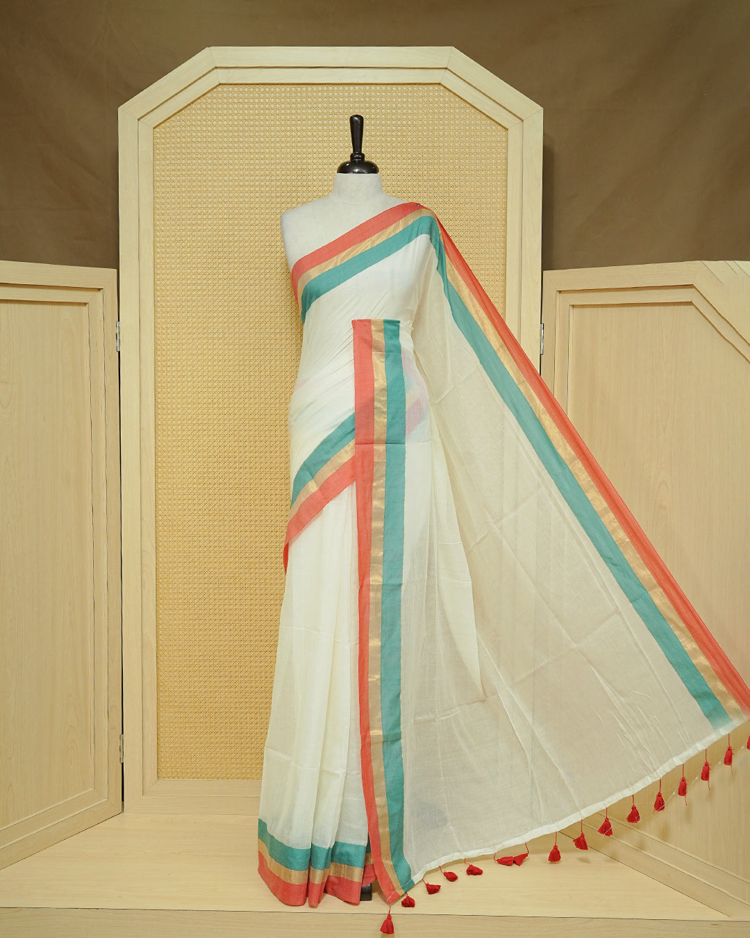 Cream colour Mul cotton saree featuring Elegant Plain body, complemented by contrast Red, Green & gold zari border & Tassels.