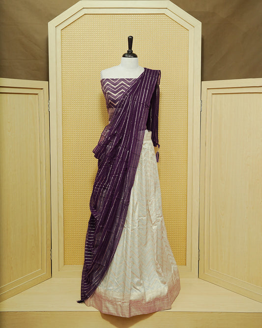 Cream colour Semi Stitched Dhavani set Featuring Gold zari Zigzag pattern With Traditional border skirt, Contrast Purple colour Dupatta, Matching blouse piece.