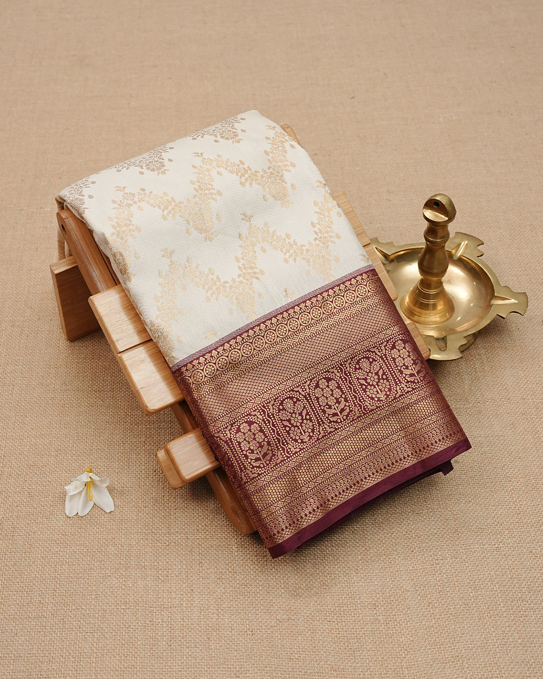 Cream colour semi wedding saree featuring gold zari Pattern on body, contrast  Dark Wine colour with traditional border, paired with matching blouse piece.