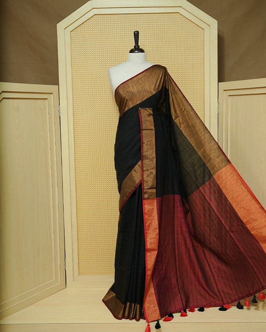 Black Colour  Mul Cotton Saree featuring an elegant plain body, complemented by a rich copper zari border and a maroon contrast pallu with red and black tassels.