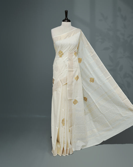 Cream colour Cotton kerala saree featuring Gold Embroidery strips with motifs on the body, complemented by a gold zari Border, paired with a matching blouse piece.