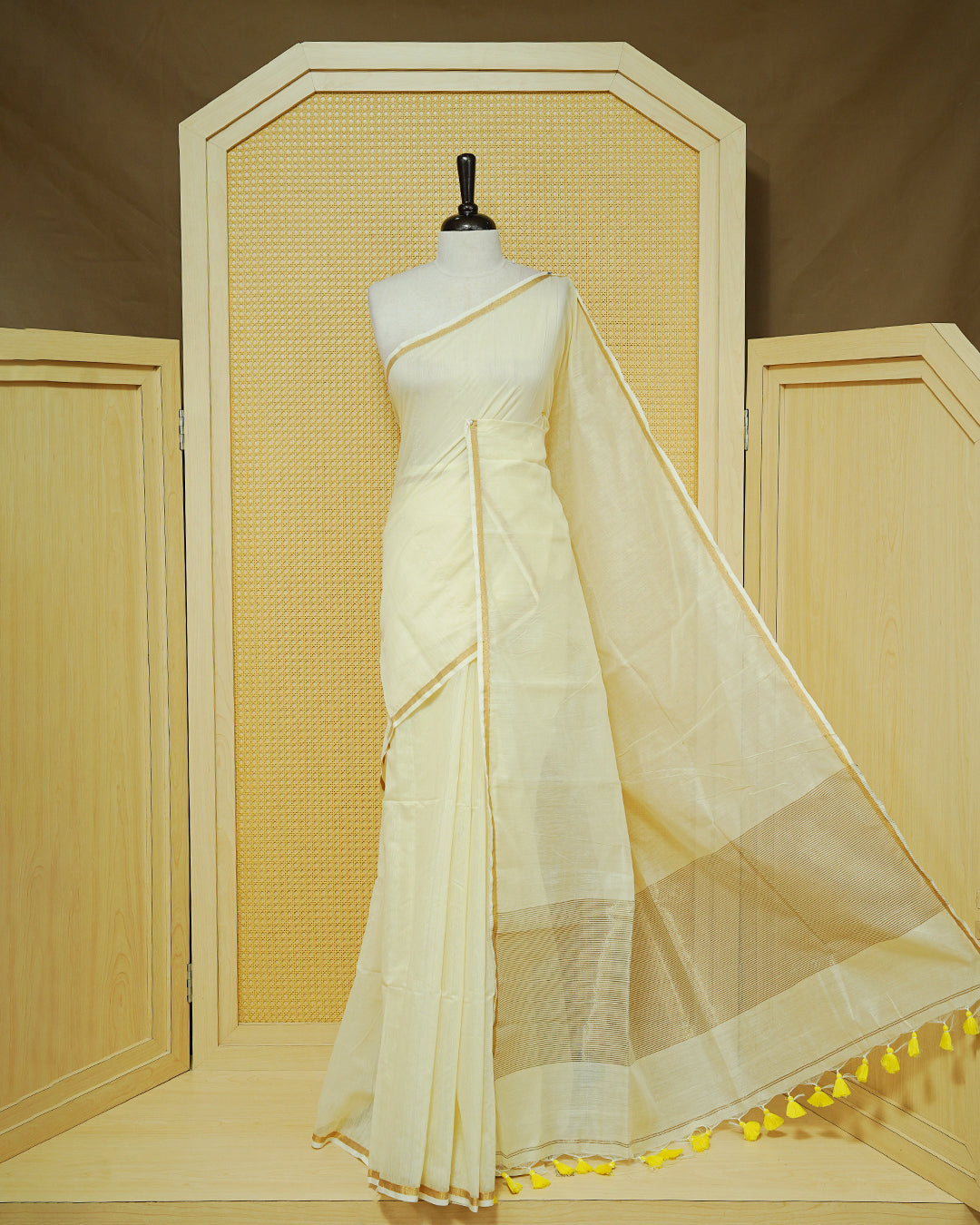 Cream Mul Cotton Saree featuring a graceful plain body with a subtle gold zari border and a finely woven striped pallu. Finished with vibrant Yellow tassels