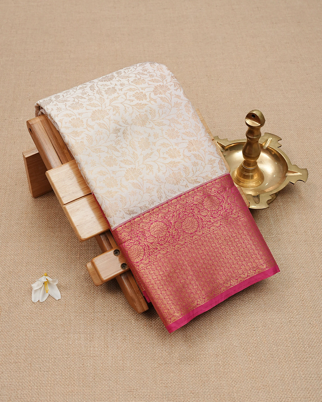 Cream colour semi wedding saree featuring gold zari Pattern on body, contrast Pink colour with traditional border, paired with matching blouse piece.