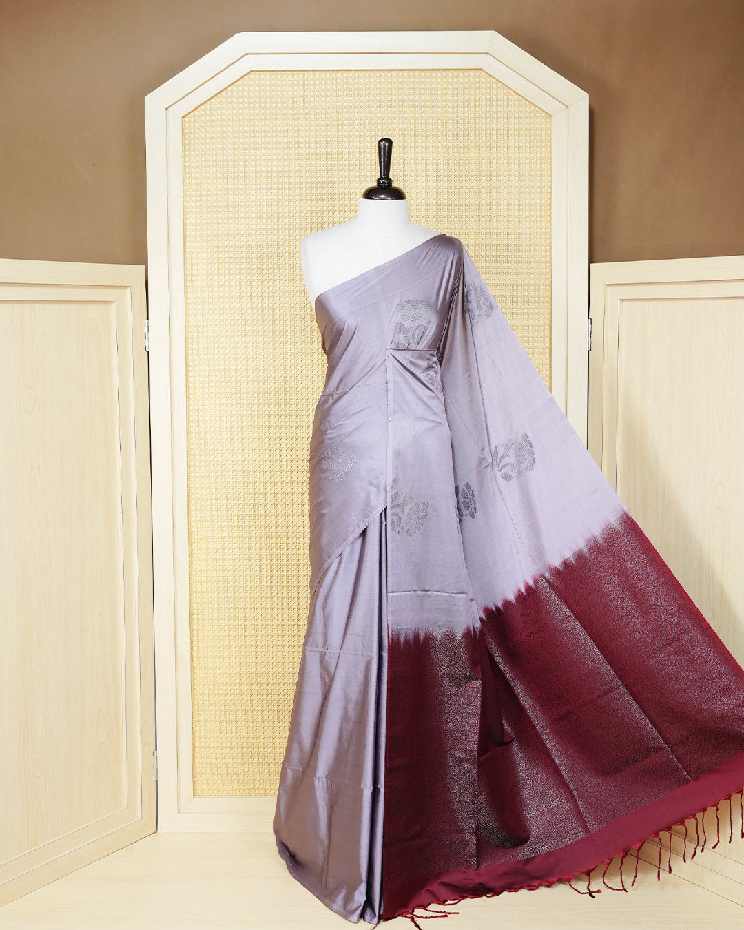 Greyish lavender colour soft silk saree featuring antique zari motifs on body with contrast dark maroon colour pallu & paired with matching blouse piece.