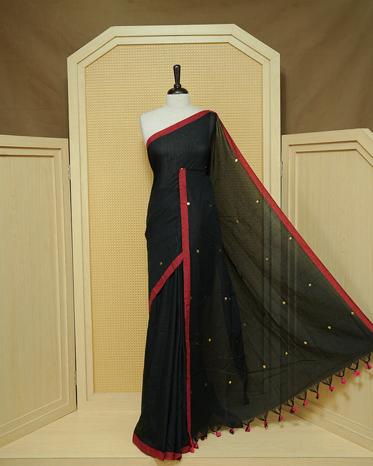 Black colour Mul cotton saree featuring Gold Sequins, complemented by Contrast Red simple Border & tassels.