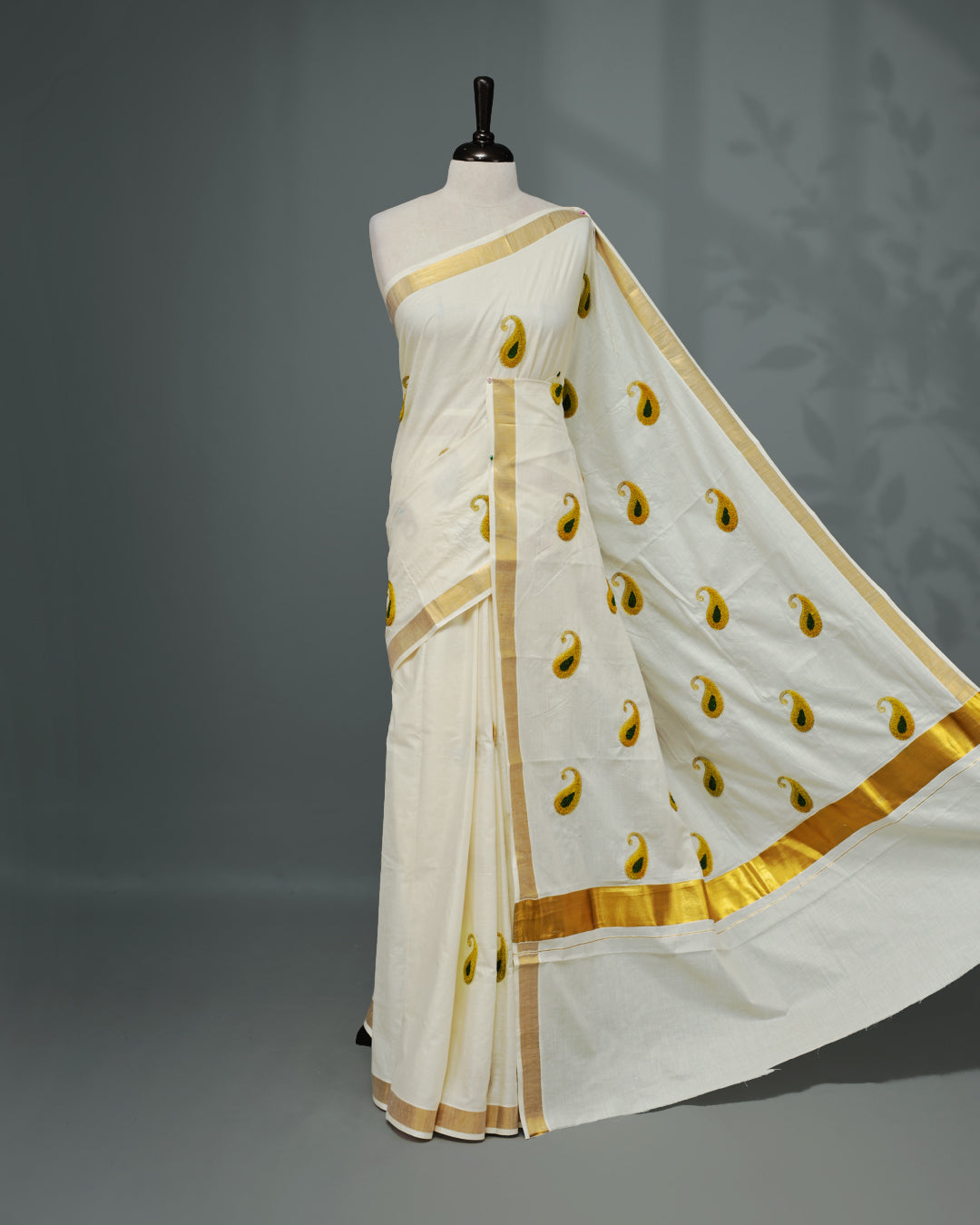 Cream colour Cotton kerala saree featuring Mango Embroidery work on the body, complemented by a gold zari Border, paired with a matching blouse piece.