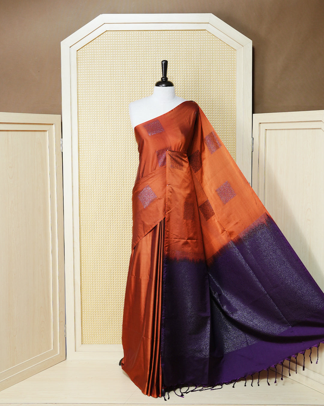 Burnt orange colour soft silk saree featuring antique zari motifs on body with contrast dark purple colour pallu & paired with matching blouse piece.