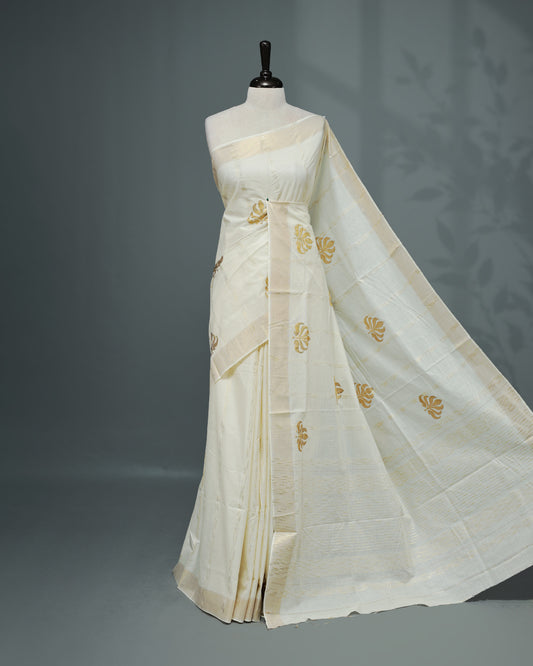 Cream colour Cotton kerala saree featuring Gold Embroidery strips with motifs on the body, complemented by a gold zari Border, paired with a matching blouse piece.