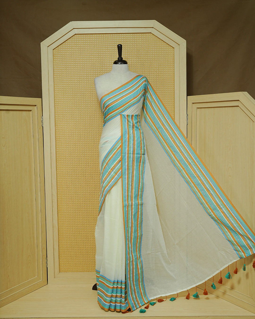 Cream colour Mul cotton saree featuring Elegant Plain body, complemented by contrast Aqua, Blue, Brown & gold zari border & Tassels.
