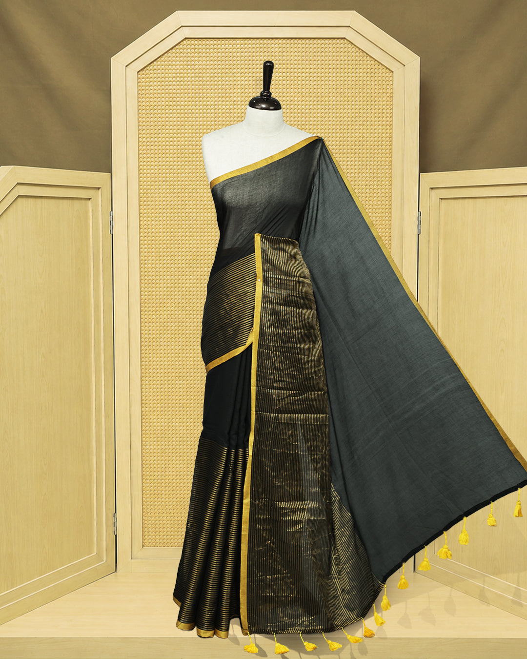 Black Mul Cotton Saree featuring an elegant plain body, beautifully complemented by a gold zari striped border and mustard-yellow tassels.