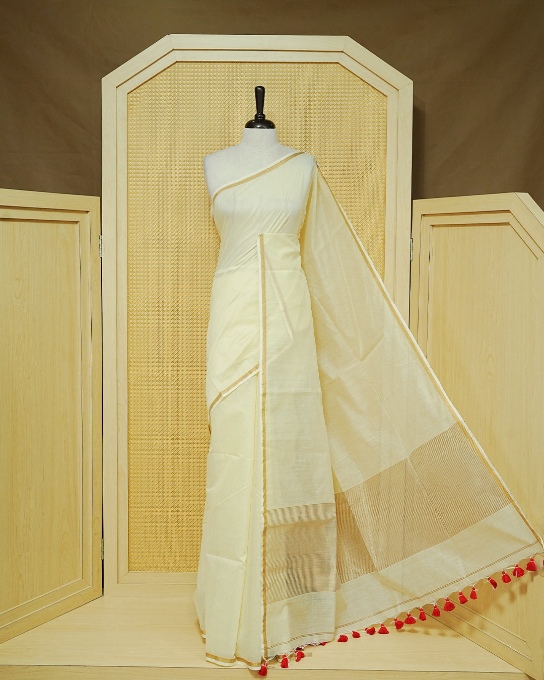 Cream Mul Cotton Saree featuring a graceful plain body with a subtle gold zari border and a finely woven striped pallu. Finished with vibrant red tassels