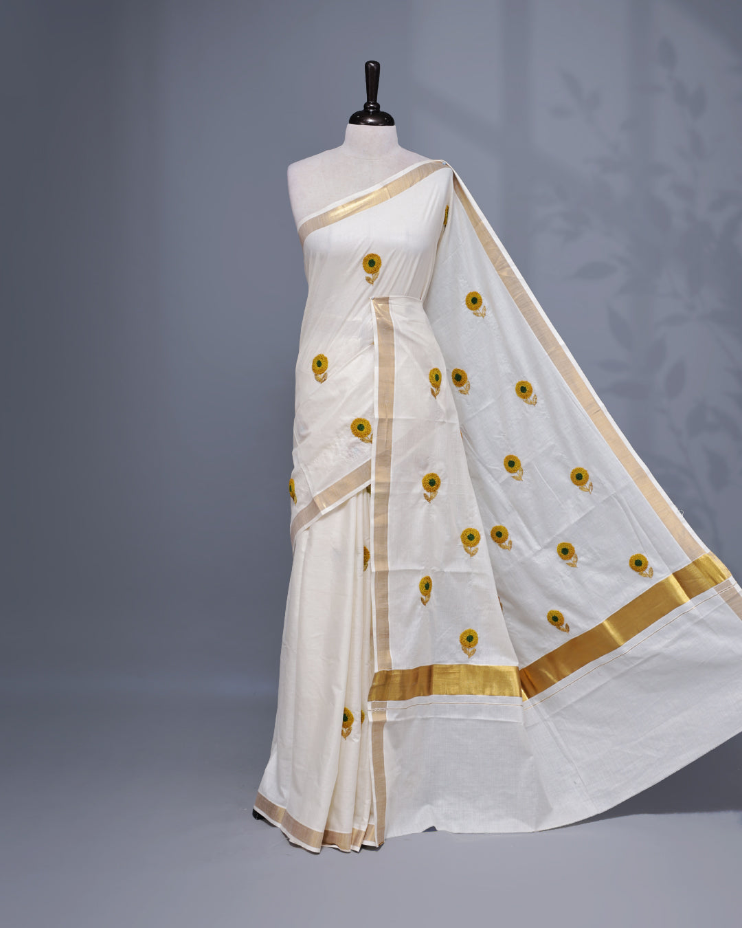 Cream colour Cotton kerala saree featuring Sunflower Embroidery work on the body, complemented by a gold zari Border, paired with a matching blouse piece.