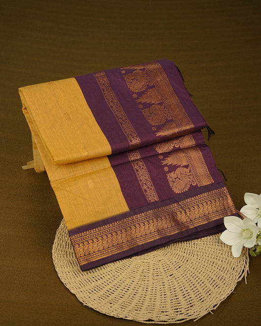 Mustard Yellow  Colour Kalyani cotton saree featuring delicate antique zari floral butta motifs on the body, complemented by a Purple contrast pallu with a rich antique zari peacock border, paired with a matching blouse piece.