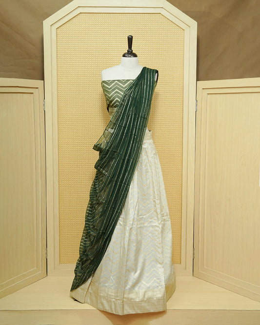 Cream colour Semi Stitched Dhavani set Featuring Gold zari Zigzag pattern With Traditional border skirt, Contrast Green colour Dupatta, Matching blouse piece.