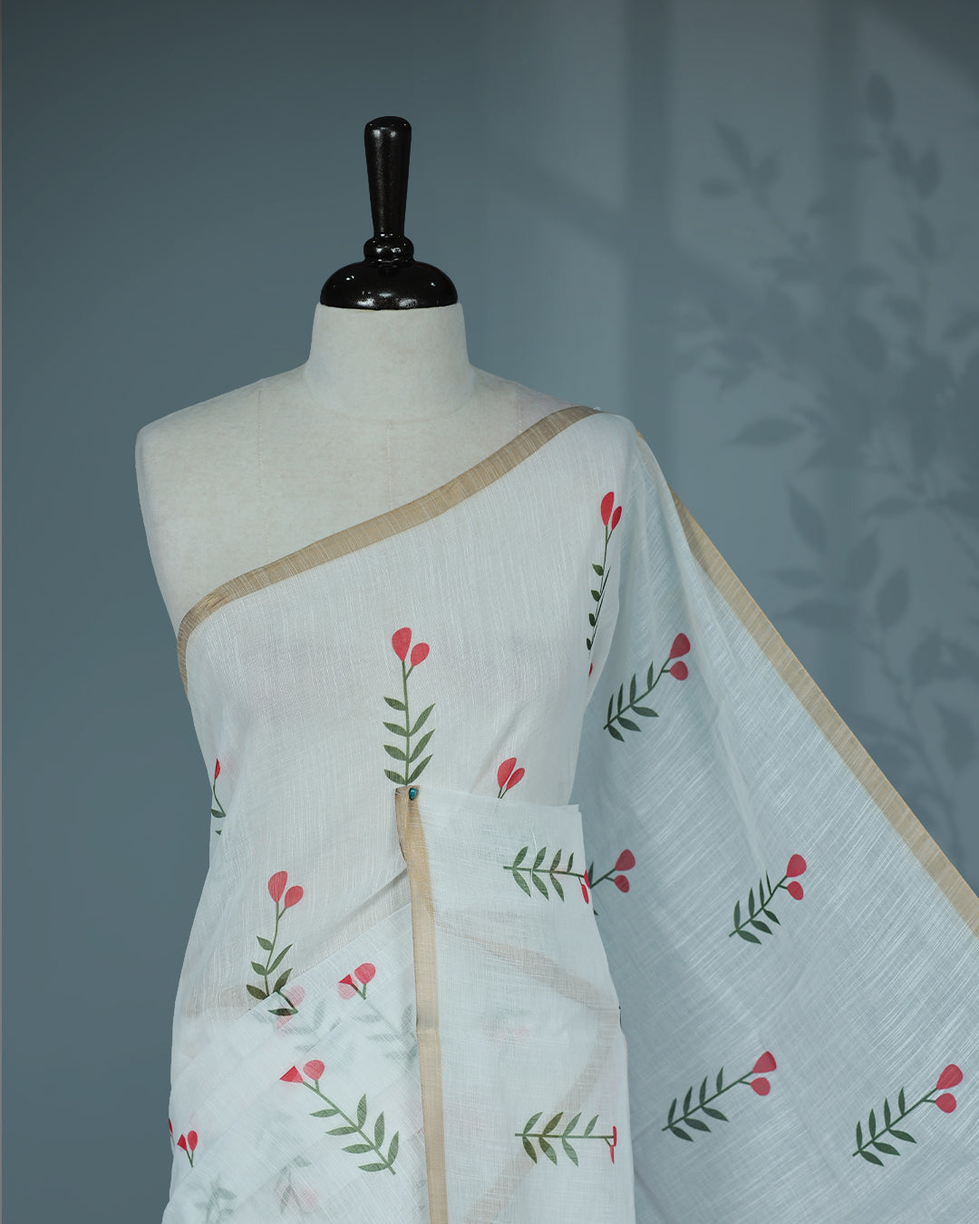 Off-white linen saree featuring beautiful Red floral and leafy prints on the body, complemented by a tissue piping border and a contrasting pallu. Paired with a matching blouse piece.