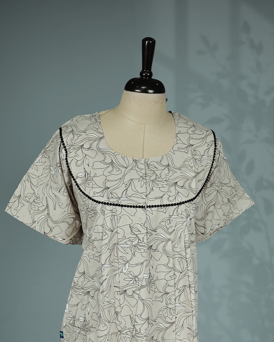 Beige & Black colour floral kodi printed nighty featuring a graceful round yoke with delicate black lace trim, soft front pleats, short sleeves and a relaxed full-length  for breathable comfort and timeless everyday style.