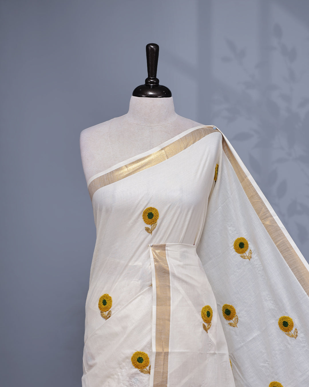 Cream colour Cotton kerala saree featuring Sunflower Embroidery work on the body, complemented by a gold zari Border, paired with a matching blouse piece.