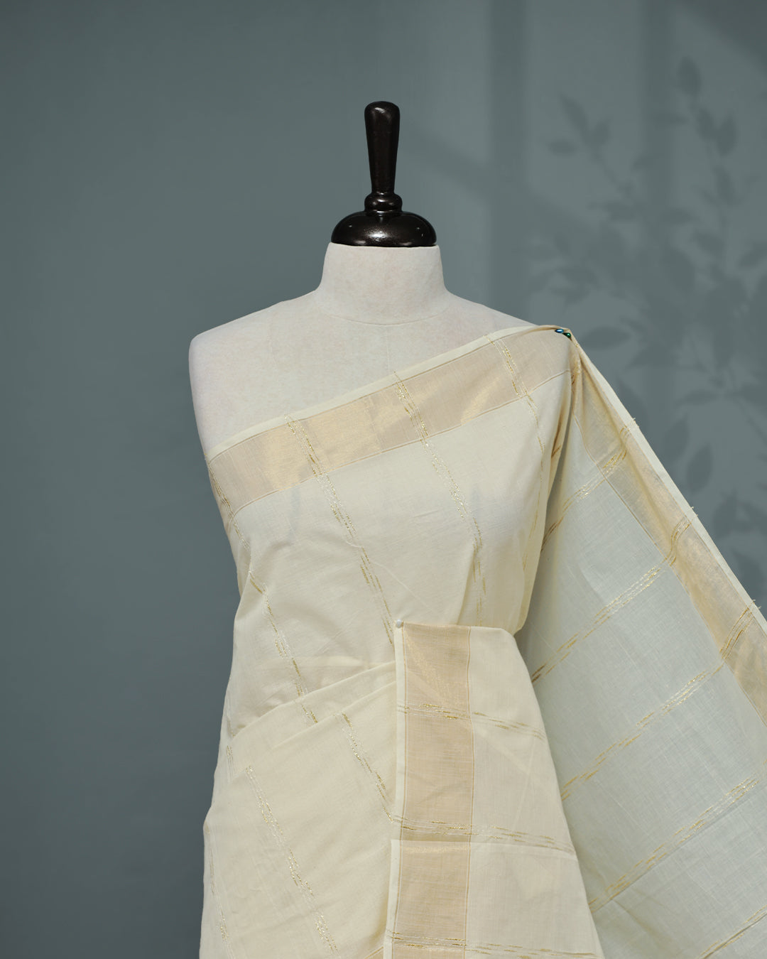 Cream colour Cotton kerala saree featuring Gold Embroidery strips on the body, complemented by a gold zari Border, red elegant tassels, paired with a matching blouse piece.