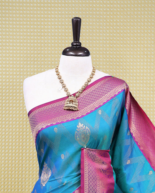 Teal colour Mulberry silk saree featuring floral gold zari patterns on body, paired with contrast Purple colour with traditional border, comes with matching blouse piece.