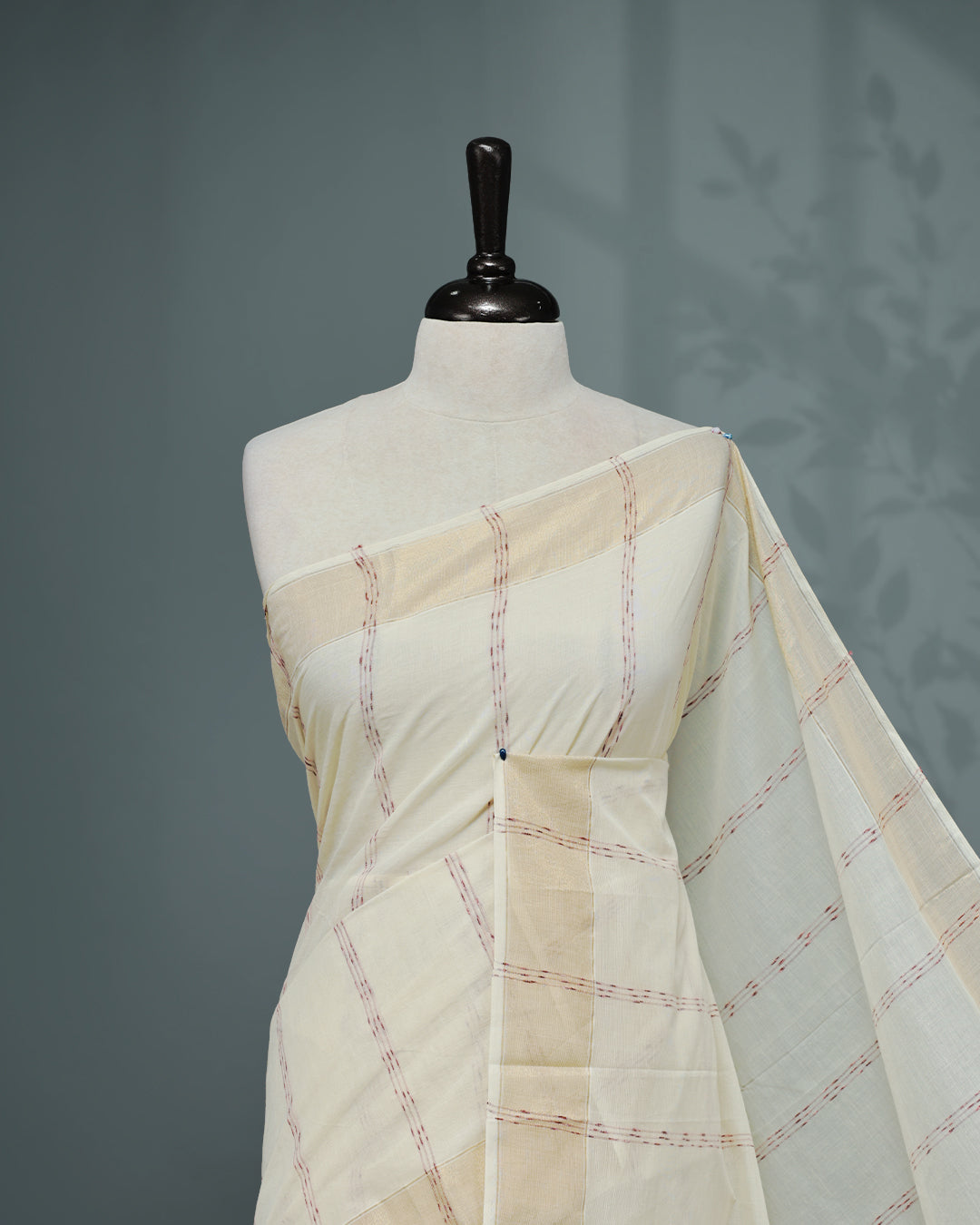 Cream colour Cotton kerala saree featuring Maroon & gold Strips on body, complemented by Gold zari Border, paired with matching blouse piece.