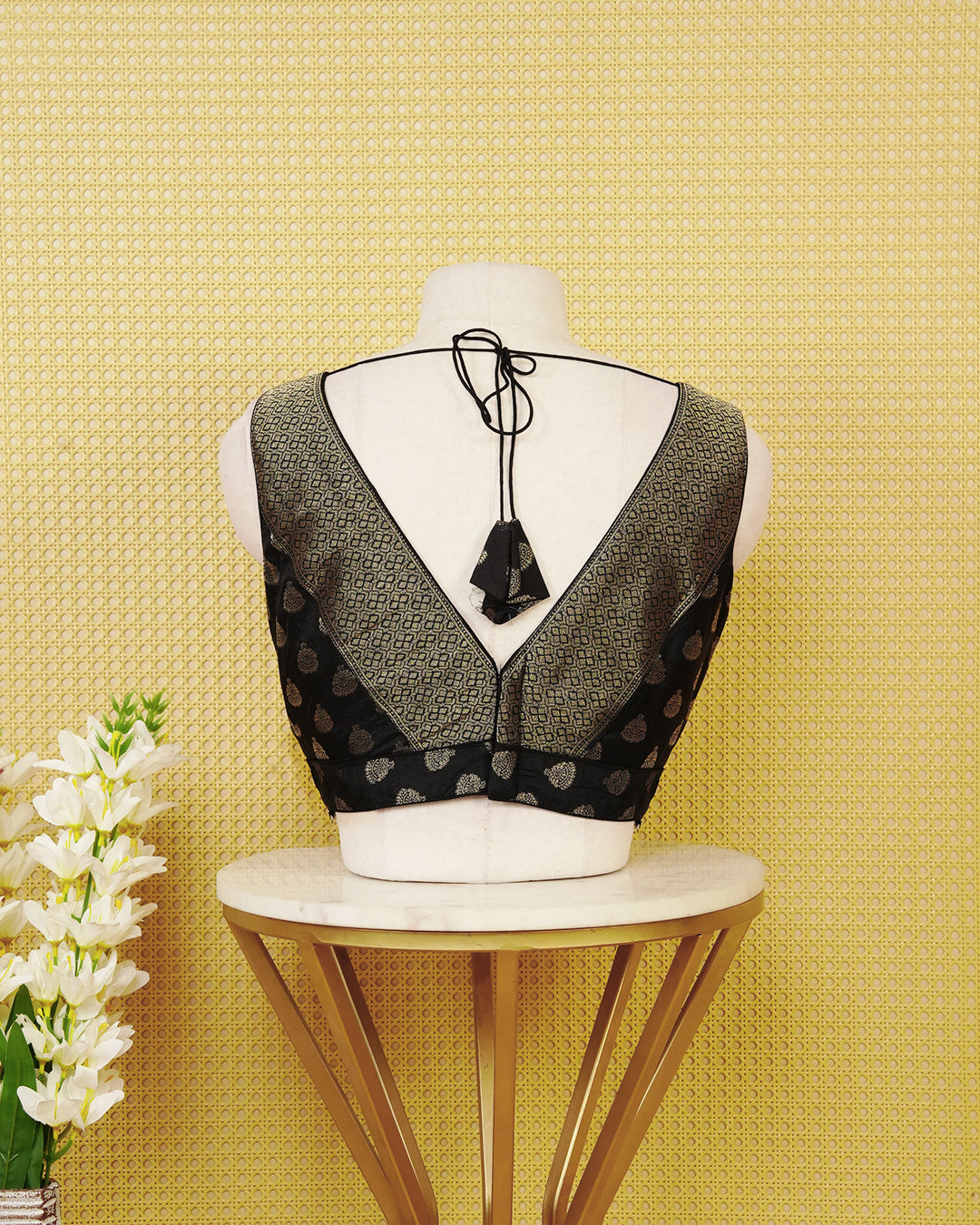 Black colour Sleeveless Blouse Featuring A Stylish V-Neck, Elegant Woven Pattern With Gold Butta Motifs, And A Comfortable Tailored Fit.