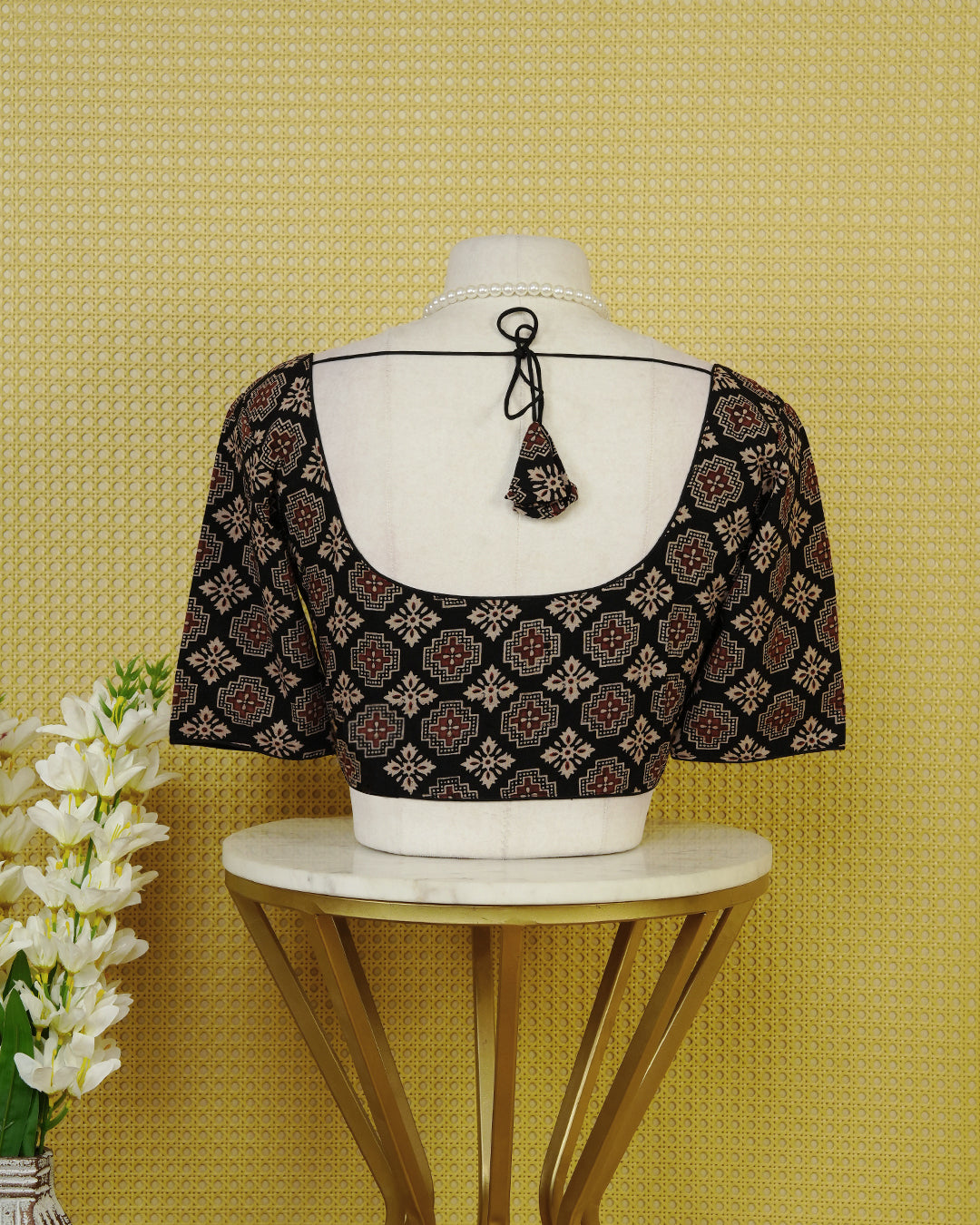 Black Colour Printed Blouse Featuring An All Over Geometric Floral Motif, Enhanced With A Round Neckline, Front Button Closure, And Elbow Length Sleeves.