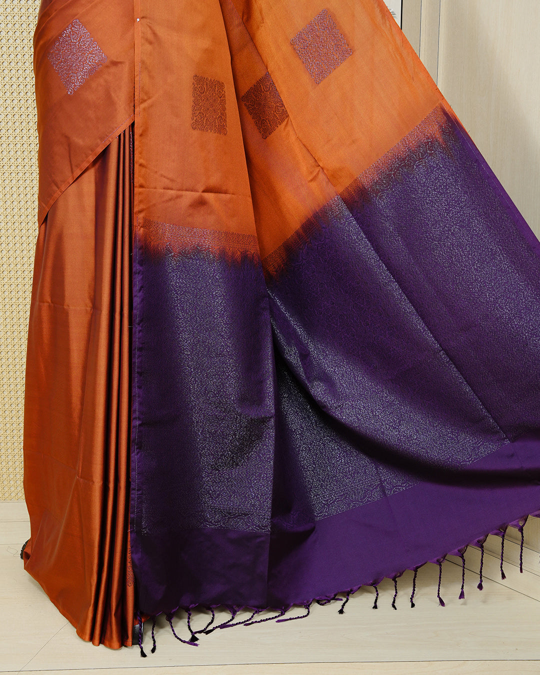 Burnt orange colour soft silk saree featuring antique zari motifs on body with contrast dark purple colour pallu & paired with matching blouse piece.