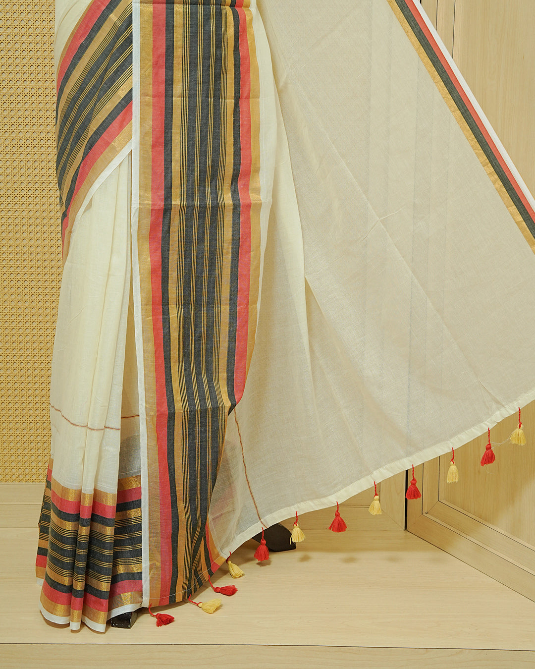 Cream colour Mul cotton saree featuring Elegant Plain body, complemented by contrast Red, Black & gold zari border & Tassels.