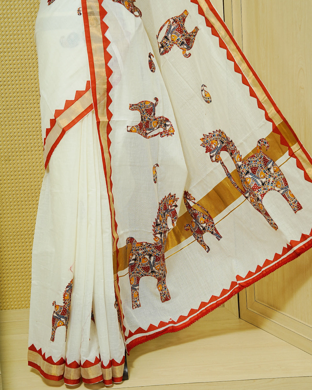 Cream colour Kerala saree Featuring Ajrakh Inspired Buttas Red Horse pattern, Gold zari border, comes with matching blouse piece.