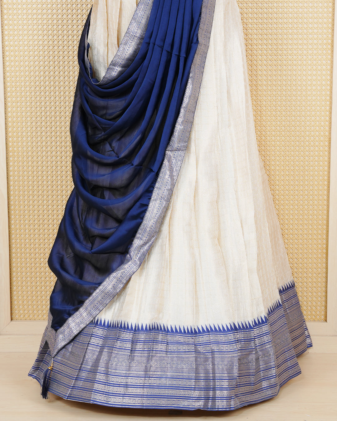 Cream colour tissue Semi stitched dhavani set featuring Gold zari check pattern with motifs on body ,contrast Blue colour with gold zari bordered skirt, paired with matching blouse piece & dupatta.