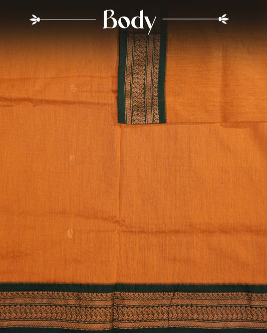Mustard Orange  Colour Kalyani cotton saree featuring antique zari floral buttas on the body, complemented by a Bottle Green contrast pallu with an antique zari peacock border, paired with a matching  blouse piece