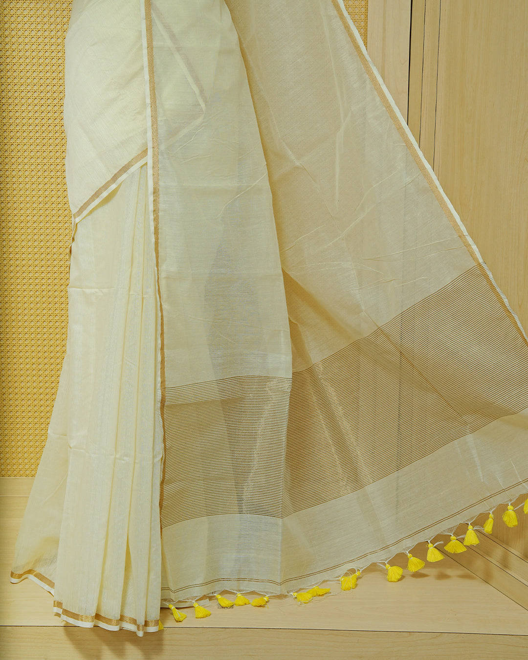 Cream Mul Cotton Saree featuring a graceful plain body with a subtle gold zari border and a finely woven striped pallu. Finished with vibrant Yellow tassels