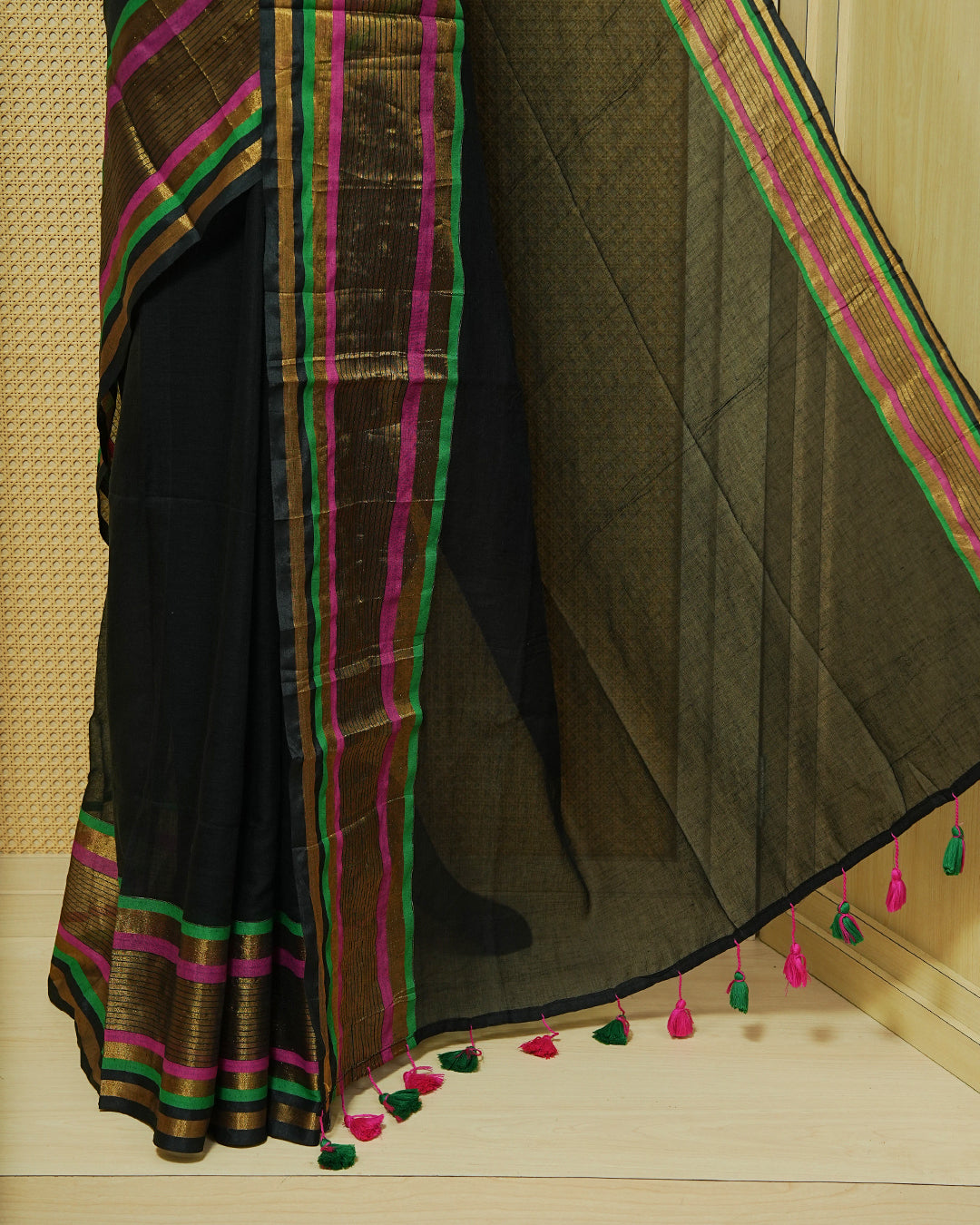 Black Mul Cotton Saree featuring a plain black body with a multicolour striped zari border in magenta, green, and gold, finished with dual-tone magenta and green tassels.
