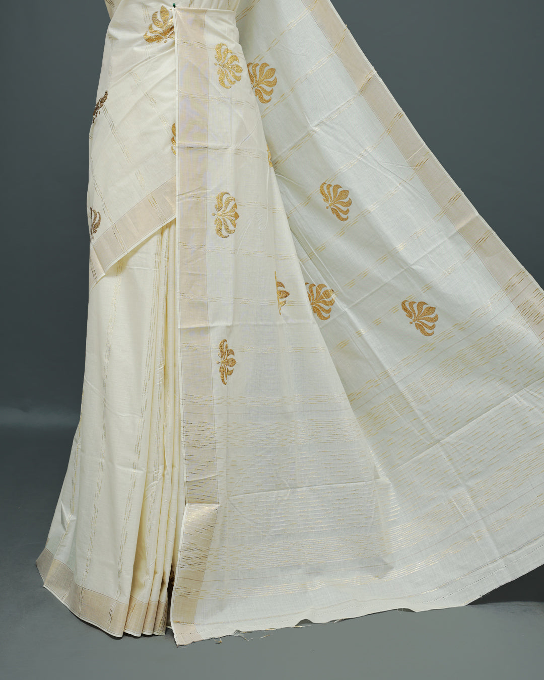 Cream colour Cotton kerala saree featuring Gold Embroidery strips with motifs on the body, complemented by a gold zari Border, paired with a matching blouse piece.