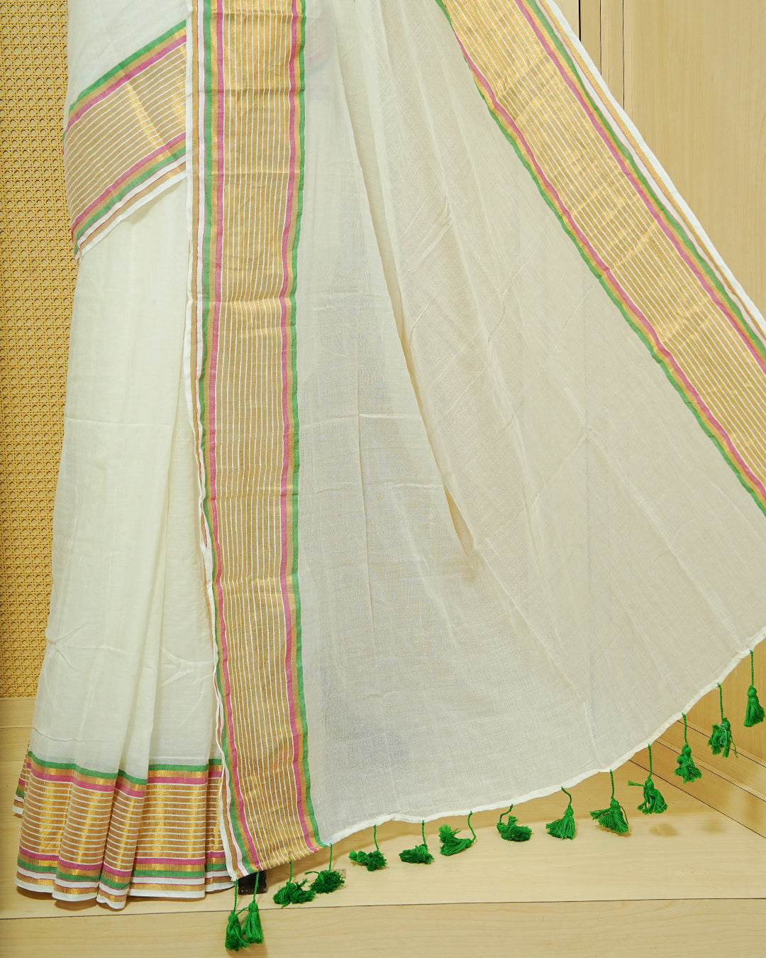 Off White Mul Cotton Saree featuring a gold zari striped border with pink and green accents, paired with a pallu and finished with green tassels.
