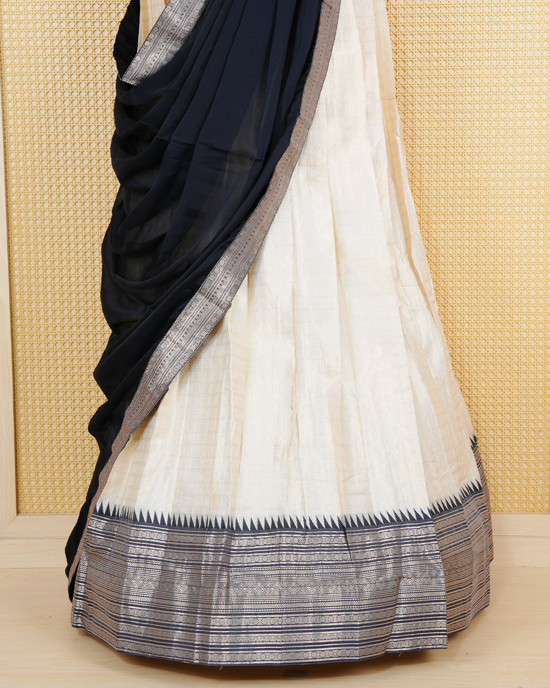 Cream colour  tissue Semi stitched dhavani set featuring Gold zari check pattern with motifs on body ,contrast Black colour with gold zari bordered skirt, paired with matching blouse piece & dupatta.