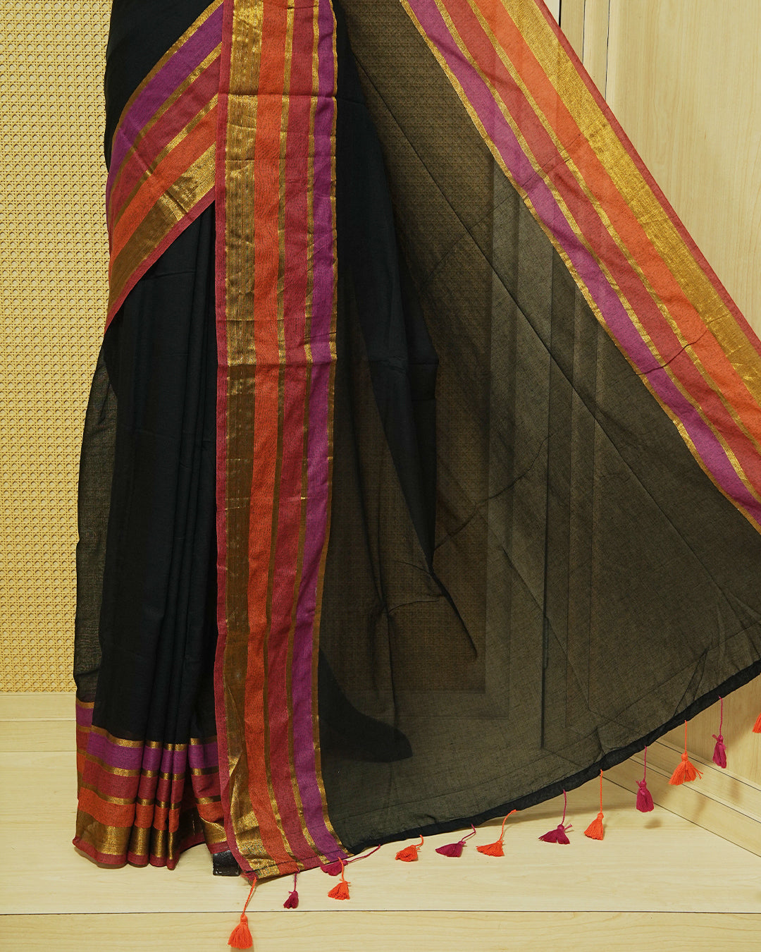 Black  Colour Mul Cotton Saree with a plain black body and a multicolour zari striped border in rust, magenta, and gold & Magenta , Orange Tassels